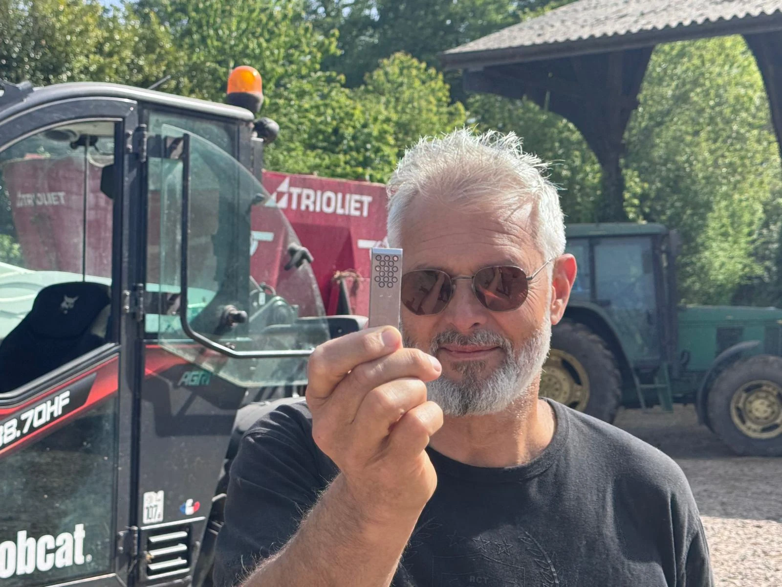 Franck Proux présentant une clé NLE devant des machines agricoles.