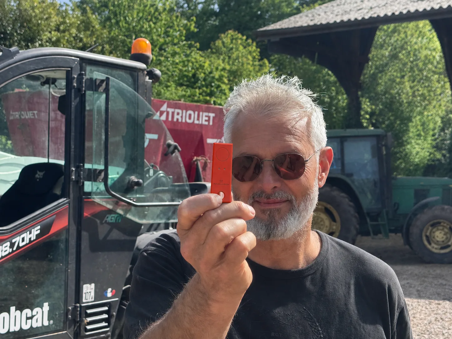 Franck Proux présentant une clé NLK devant des machines agricoles.